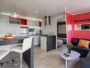 Eine moderne Küche mit einer zentralen Kochinsel, ein Essbereich mit Barhocker, ein Wohnbereich mit Sofa und Couchtisch sowie ein an der Wand montierter Fernseher.