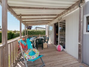 Ein überdachter Außenbereich mit einer Holzterrasse, einem Tisch mit Stühlen und einem Strandball.