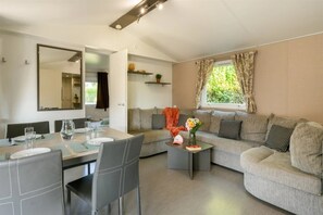 Ein modernes Wohnzimmer mit Essbereich, einer Sofagarnitur, einem Couchtisch und einem großen Fenster mit Vorhängen.