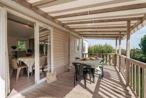 Ein überdachter Außenbereich mit Tisch und Stühlen, einer Holzterrasse und Blick ins Grüne.