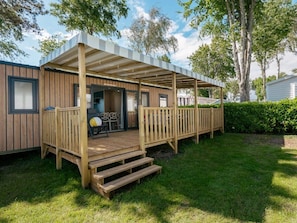 Eine Holzterrasse mit überdachter Sitzgelegenheit, einem kleinen Tisch und einem Stuhl.