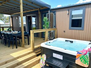 A hot tub with steps leading up to it, a covered patio area with a table and chairs, and a wooden deck. - Camping 4 étoiles - Parc aquatique - ccbg0ch (Guidel)