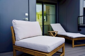 Two wooden lounge chairs with white cushions on a balcony with a glass door leading to a garden. - 3-bedroom townhome in peaceful Seattle with AC for relaxing stays (Seattle)