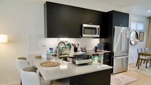 Ett modernt kök med en central köksö, rostfria vitvaror och en matplats med bord och stolar.