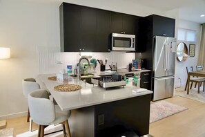 A modern kitchen with a central island, stainless steel appliances, and a dining area with a table and chairs. - 3-bedroom townhome in peaceful Seattle with AC for relaxing stays (Seattle)