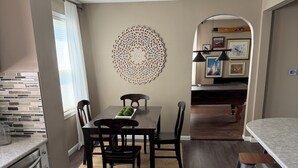 Uma cozinha moderna com piso de madeira escura, área de jantar com mesa e cadeiras, um painel decorativo e vista para a sala de estar.