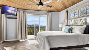 A bedroom with a bed, a ceiling fan, a TV, and a view of the outdoors. - Mtn Views, Game Room, Near Dollywood & Gatlinburg, Firepit, Hot Tub, Bunk Beds (Sevierville)