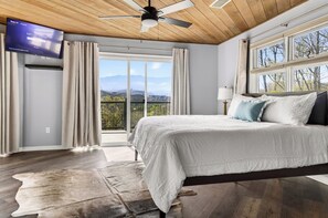 Ein Schlafzimmer mit Bett, Deckenventilator, Fernseher und Blick ins Freie.