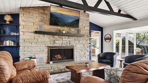 A stone fireplace with a mounted TV, leather sofas, and a wooden coffee table in a room with a view. - Mtn Views, Game Room, Near Dollywood & Gatlinburg, Firepit, Hot Tub, Bunk Beds (Sevierville)