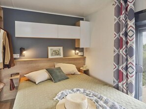 Ein Schlafzimmer mit Bett, Nachttischen, einem Kopfteil, einem gerahmten Bild und einem Fenster mit Vorhängen.