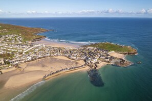 An aerial view of a coastal town with a beach, a fortified structure, and a mix of residential and commercial buildings. - Hidden 16- Garden Apartment (St Ives)