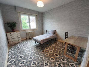 Une chambre Ă coucher avec un lit, une commode, un radiateur, une fenĂȘtre et une plante en pot.
