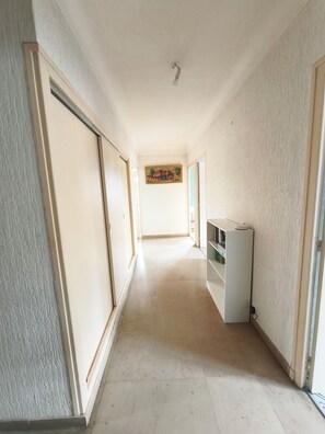 A hallway with a ceiling light, a painting on the wall, and a refrigerator.