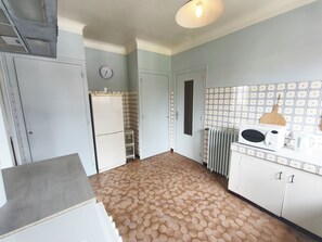 A kitchen with a hexagonal tile floor, a white refrigerator, a microwave, and a clock on the wall.