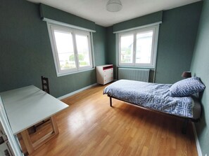 Une chambre avec un lit, un bureau et deux fenĂȘtres.