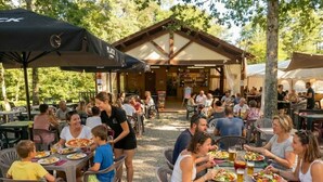 Un área de comedor al aire libre con mesas y sillas, un espacio de estar cubierto y un edificio al fondo.