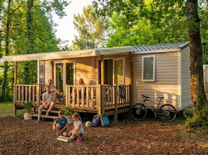 Eine kleine Holzhütte mit Veranda, einem Fahrrad und einigen Personen, die draußen sitzen.