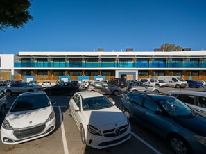 A parking lot with multiple cars, a building with large windows and a blue facade, and a clear blue sky. - Sunset Loft By CanariasGetaway (Mogán)