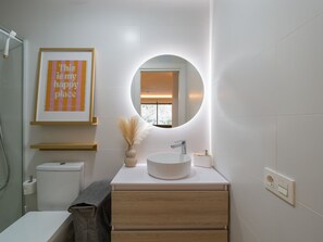 A modern bathroom with a round mirror, a white sink, and a framed picture on the wall. - Sunset Loft By CanariasGetaway (Mogán)