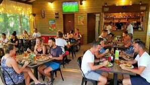 Un restaurante con paredes, mesas y sillas de madera, y una zona de bar con botellas.