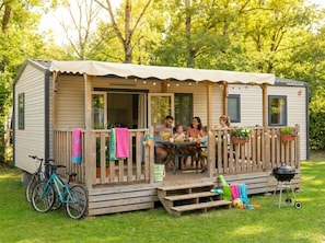 Ein Mobilheim mit Terrasse, Sitzgelegenheit im Freien, Grill und einem Fahrrad.