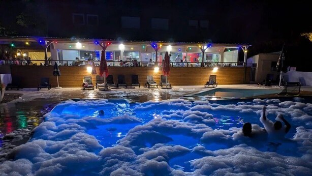 Una piscina con agua y espuma, rodeada de sillas de descanso y un edificio con luces.