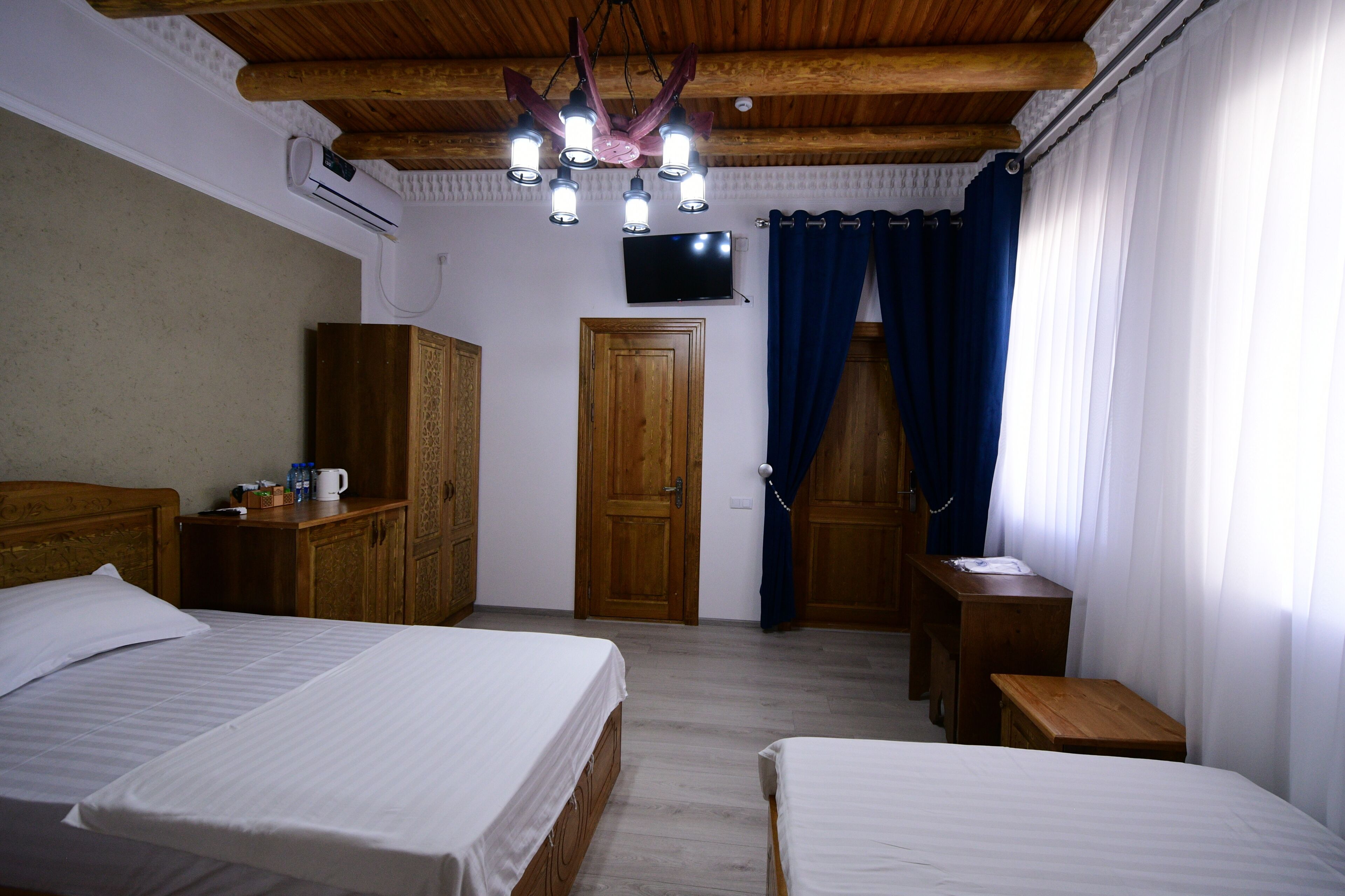 Habitación con dos camas, techo de madera, televisor y una puerta con cortinas.