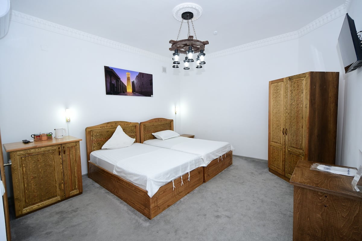 A bedroom with a wooden bed, a wardrobe, a desk, a television, and a wall-mounted picture.
