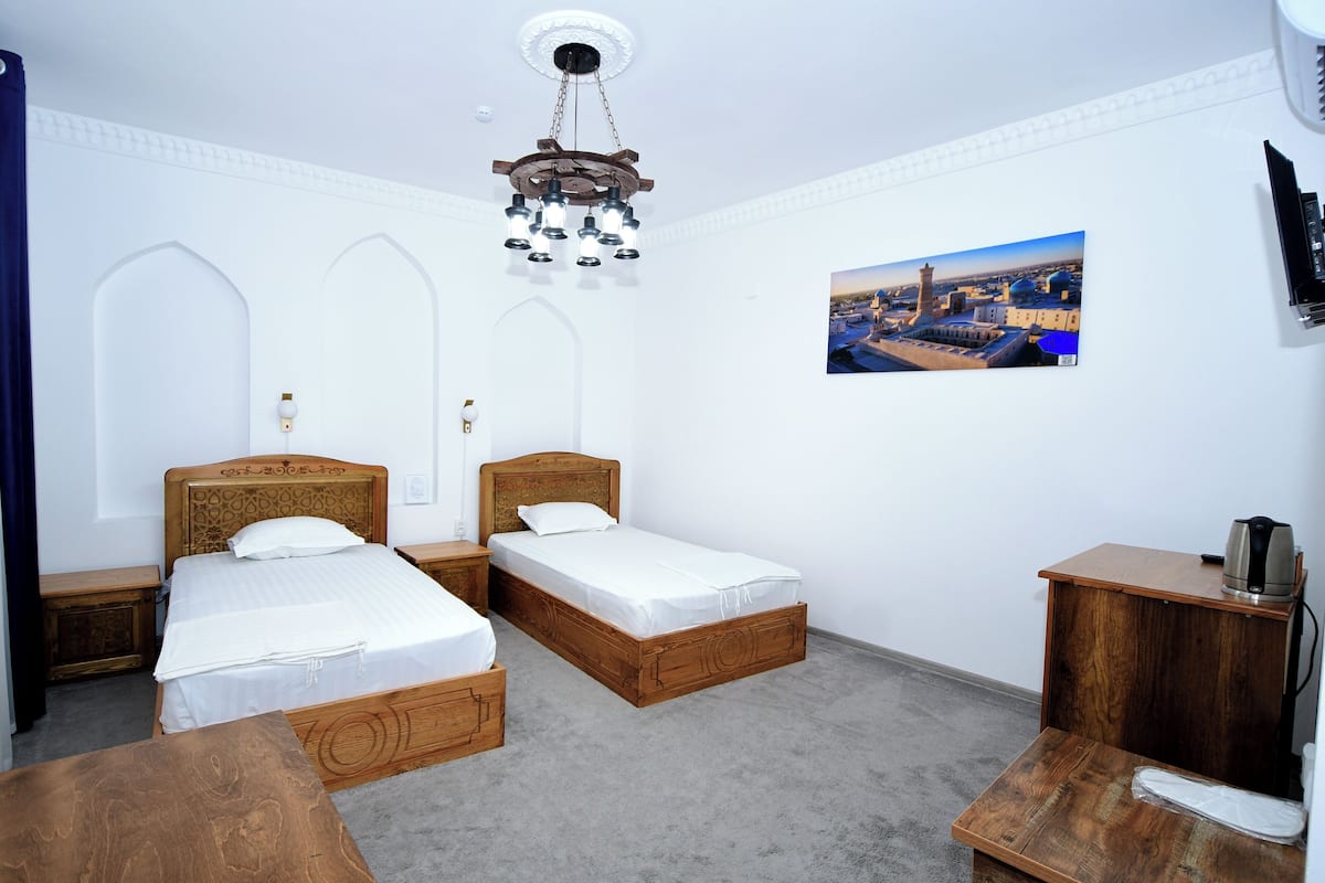 A room with two wooden beds, a wooden nightstand, a small table, a wall-mounted picture, and a ceiling light fixture.
