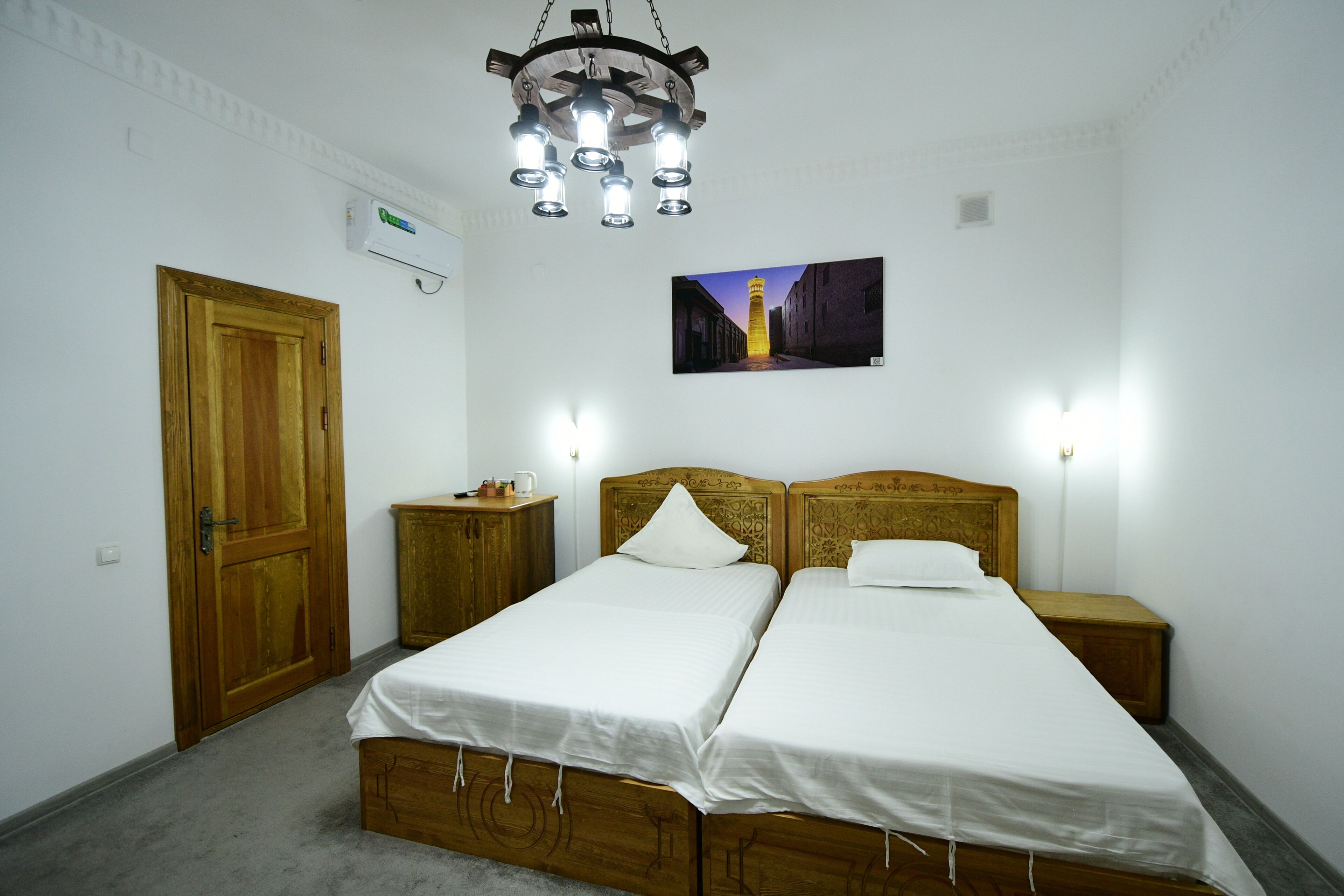 A room with two wooden beds, a wooden door, a wall-mounted air conditioner, a framed picture, and a hanging light fixture.