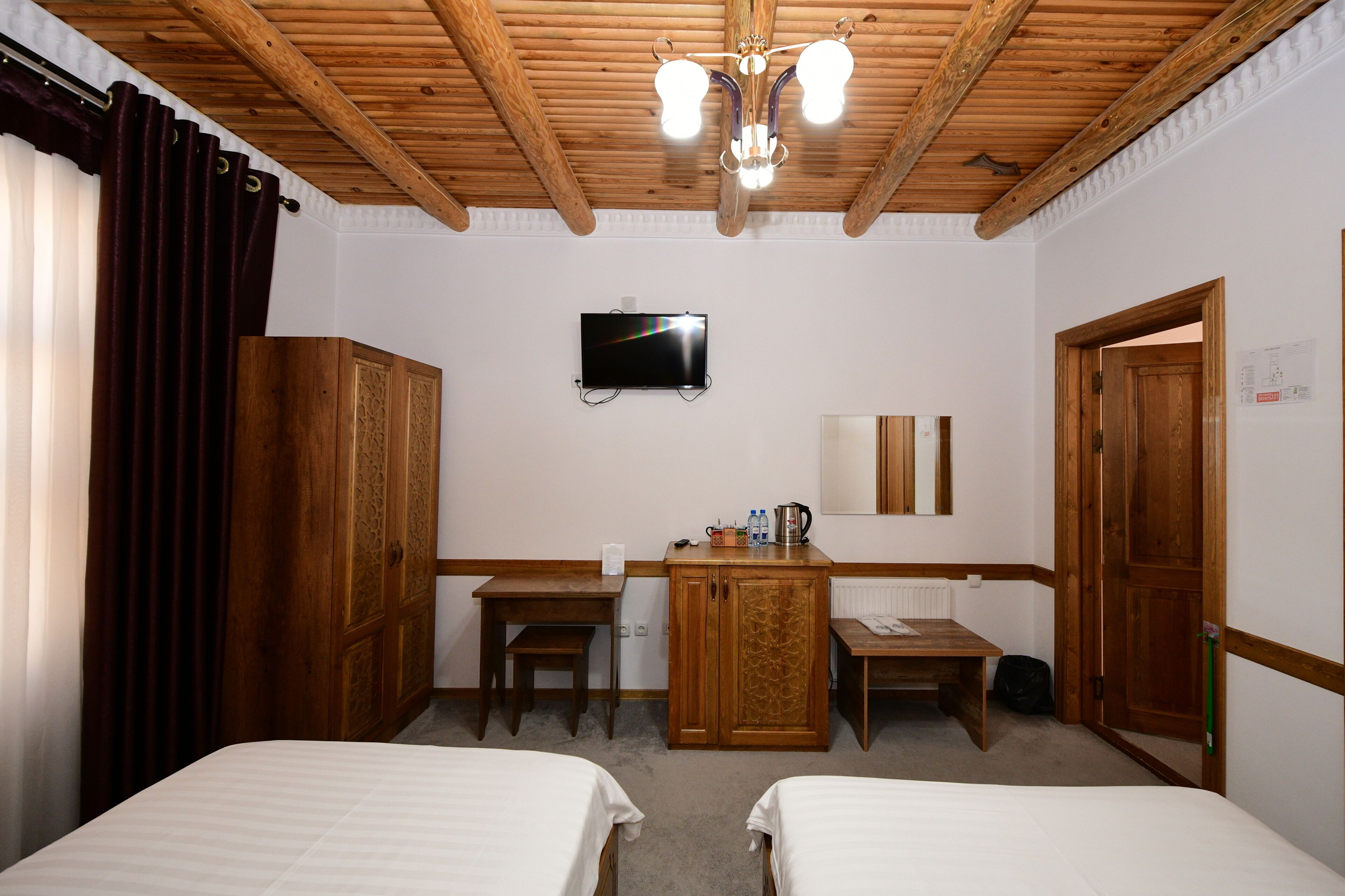A hotel room with two beds, a wooden desk, a television, and a wooden wardrobe.