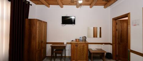 A hotel room with two beds, a wooden desk, a television, and a wooden wardrobe.