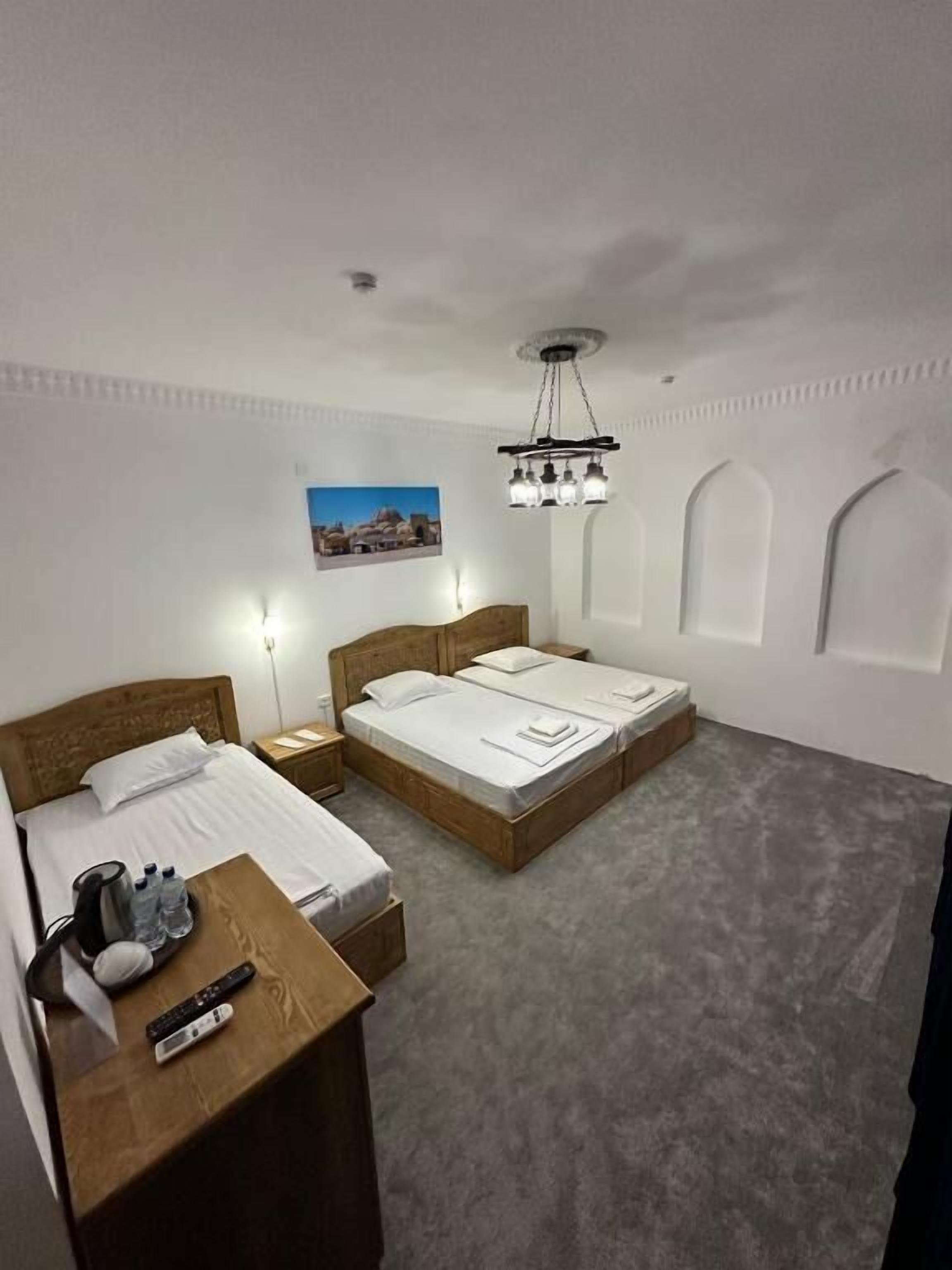 A hotel room with two beds, a wooden nightstand, a desk with a chair, a chandelier, and a wall-mounted picture.