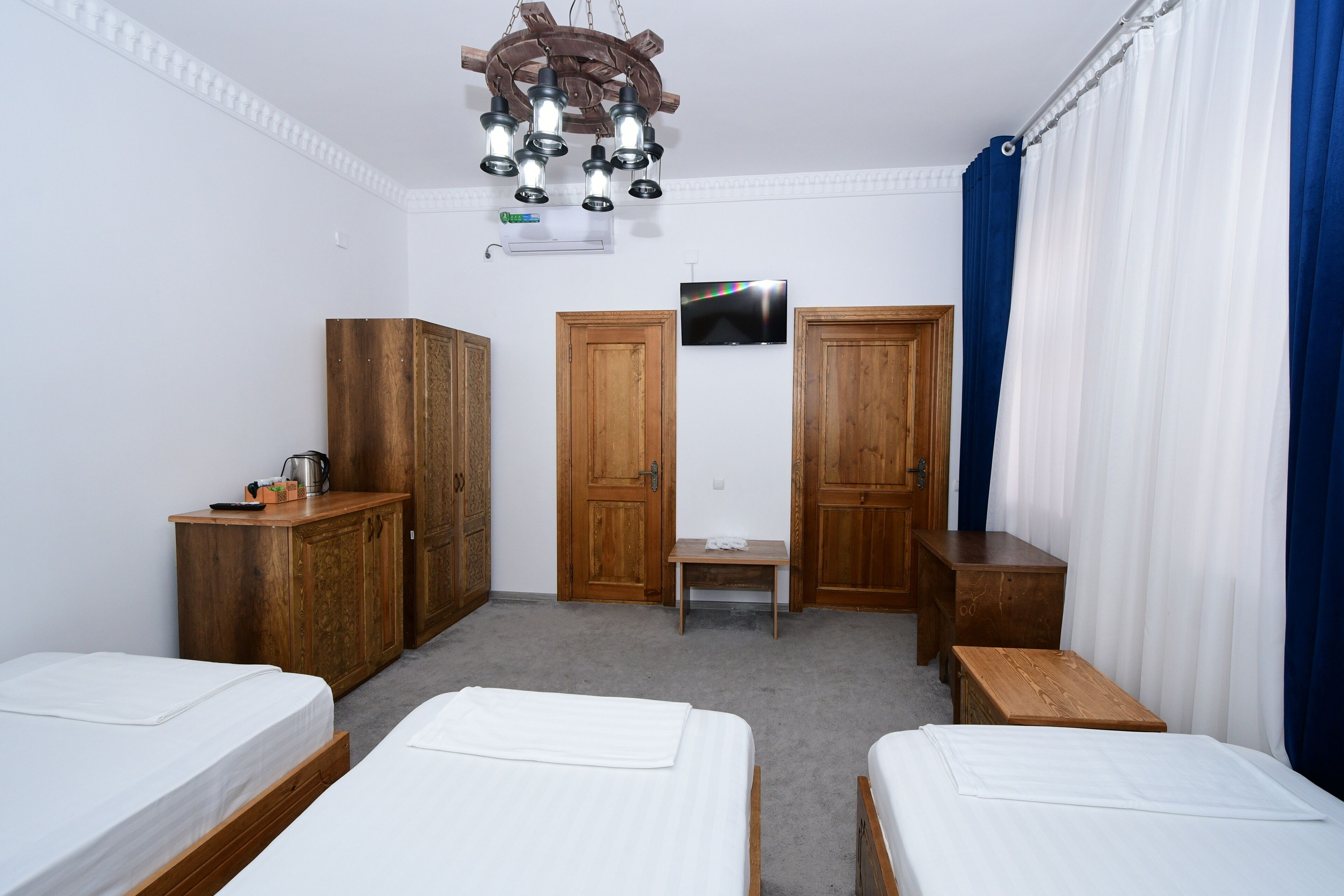 A hotel room with two single beds, wooden wardrobes, a small table, a television, and a ceiling light fixture.