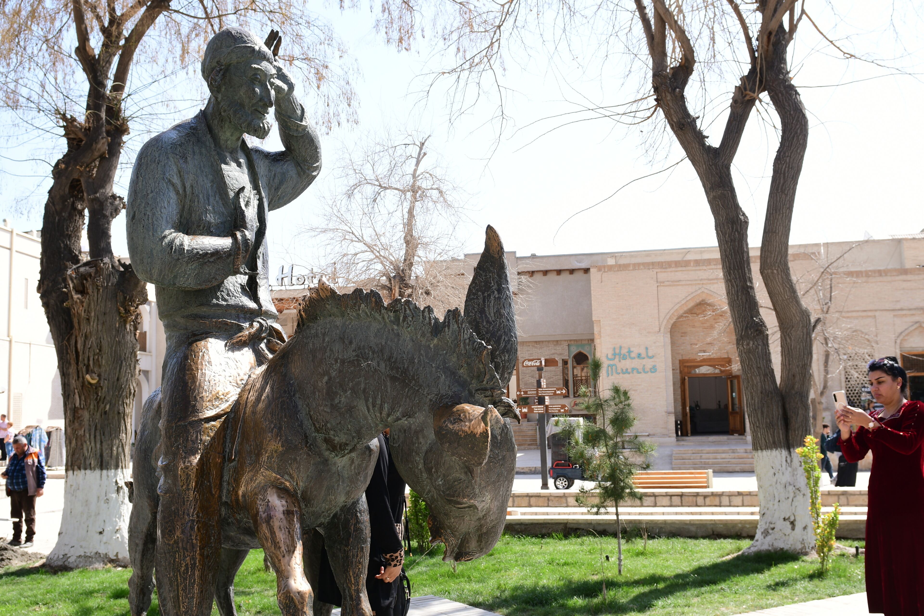 A statue of a man on a horse in a public square with trees and a building in the background.