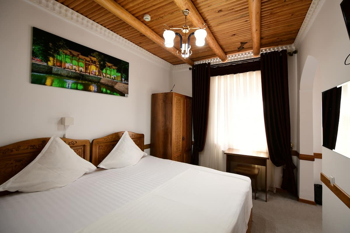 A hotel room with a bed, a desk, a wardrobe, and a painting on the wall.