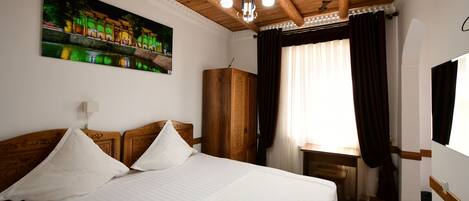 A hotel room with a bed, a desk, a wardrobe, and a painting on the wall.