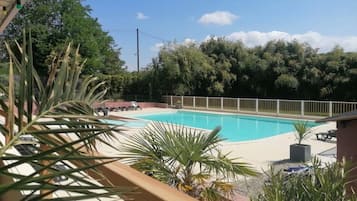 Une piscine dotée d’une terrasse en bois, entourée de verdure et d’une clôture.