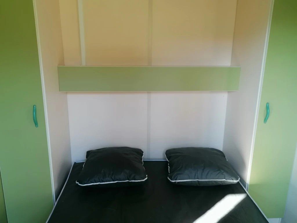 A small, single-bed room with a green wall and a white ceiling. There are two black pillows on the bed.