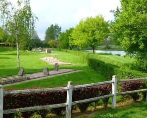 Ein Park mit befestigten Flächen, einem Gewässer und einem Holzzaun.
