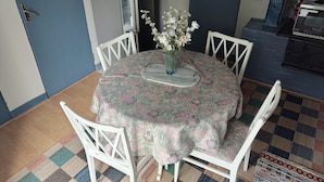 Un comedor con una mesa redonda, sillas blancas, un mantel floral y un jarrón con flores.