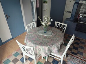 Ein Essbereich mit einem runden Tisch, weißen Stühlen, einer blumigen Tischdecke und einer Vase mit Blumen.