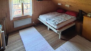 Una habitación tipo cabaña de madera con una cama, una ventana, un radiador y un ventilador de techo.