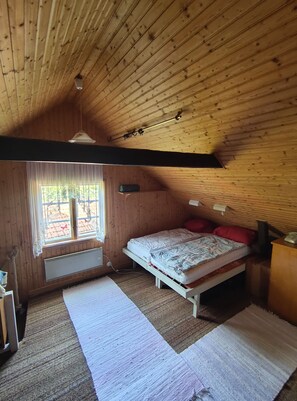 Une pièce de style cabane en bois, comprenant un lit, une fenêtre, un radiateur et un ventilateur de plafond.