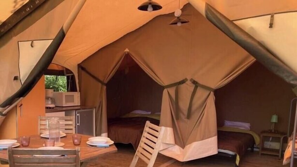 Ein Zelt mit Esstisch und Stühlen, einem Bett und einer kleinen Küchenzeile.