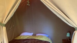Ein Zeltraum mit Bett, Kissen, Nachttisch und Lampe.