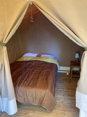A tented room with a bed, pillows, a nightstand, and a lamp. - Camping 3 étoiles - Piscine  - ccbfghg (Mamers)