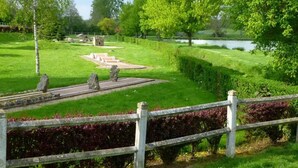 Ein Park mit befestigten Flächen, einem Gewässer und einem Holzzaun.