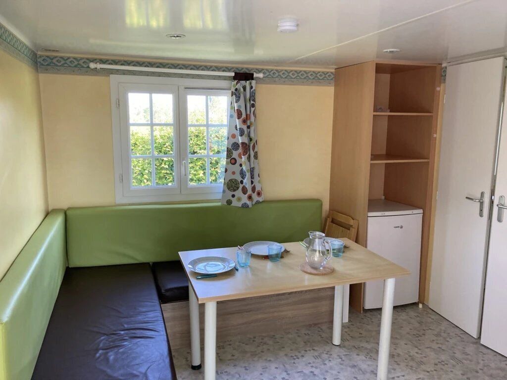 Ein Zimmer mit einem grünen Sofa, einem kleinen Tisch mit Tellern und Gläsern, einem Fenster mit Vorhang und einem Schrank.