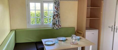 Ein Zimmer mit einem grünen Sofa, einem kleinen Tisch mit Tellern und Gläsern, einem Fenster mit Vorhang und einem Schrank.